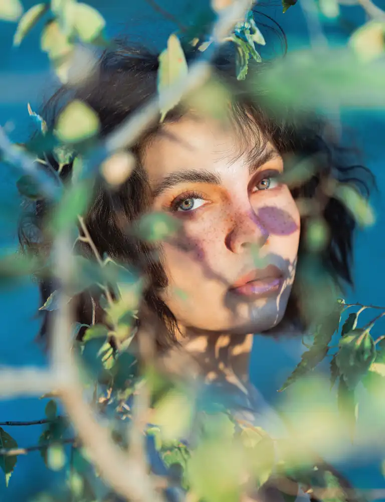 Soft portrait of a woman in the nature, covered by the ambiant shadows of the leaves around her