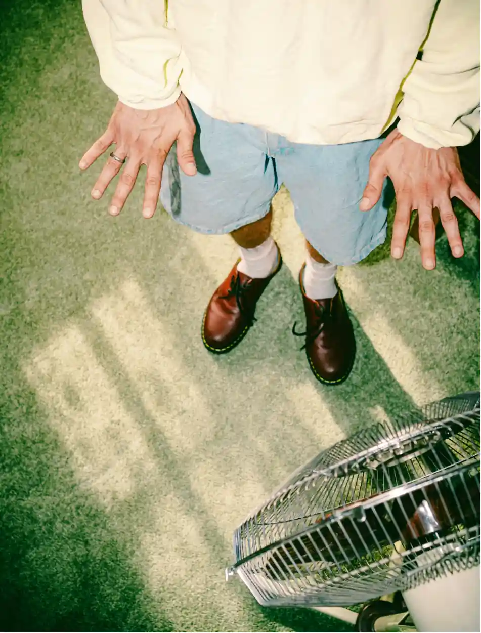 Man standing on a green carpet, showing his ring, with a ventilator on foreground, super retro vibes