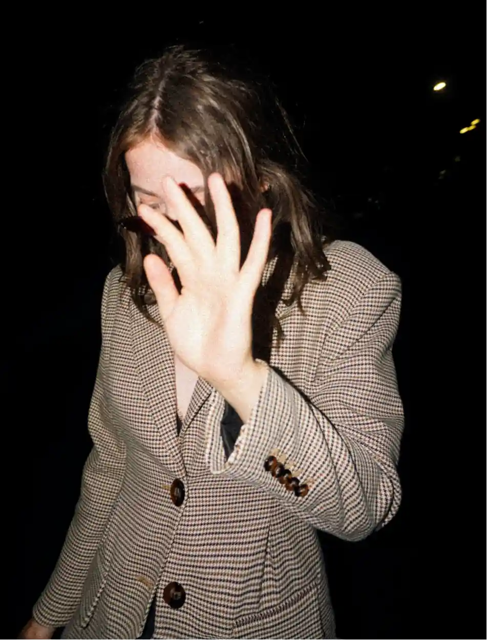 Paparazzi like picture of woman dressed in a suit, hiding her face with her hand